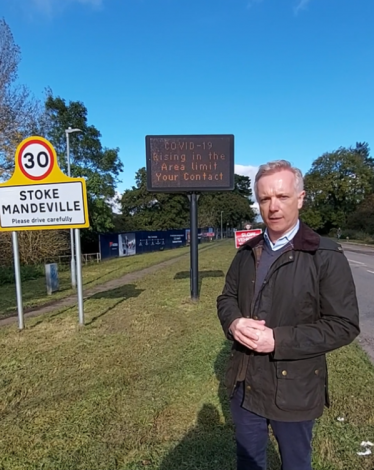 Rob in Stoke Mandeville next to sign reminding residents to follow Covid-19 rules